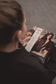 A woman reading a fashion magazine featuring celebrity photos, seen from behind.