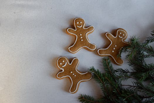 Three gingerbread men cookies with frosting on a surface next to pine leaves.