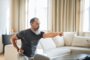 Elderly man with a beard performing yoga poses indoors, promoting health and wellness.