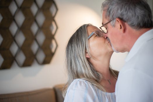 A tender moment between a senior couple kissing indoors, showcasing love and affection.