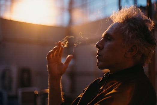 Senior man sitting and smoking indoors, captured with backlit lighting.