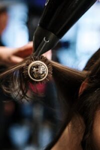 Close-up of a hairstylist styling hair with a brush and dryer in a salon setting.