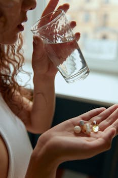 Close-up of a woman holding pills and a glass of water indoors.